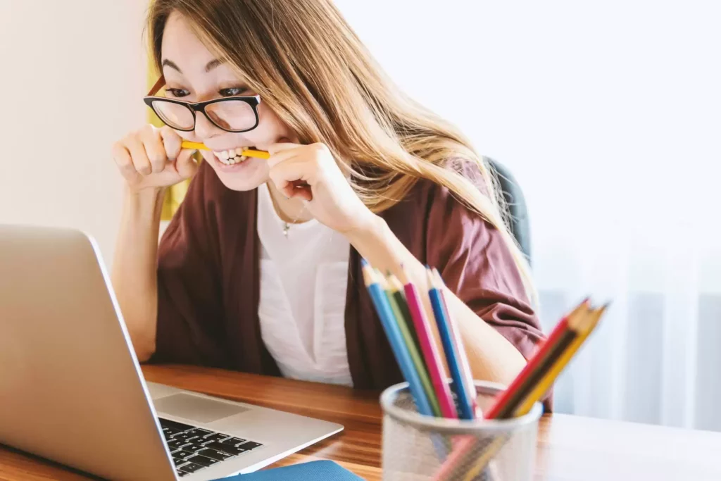 A woman with a pencil in her mouth looking at a computer feeling stressed about construction bookkeeping tasks